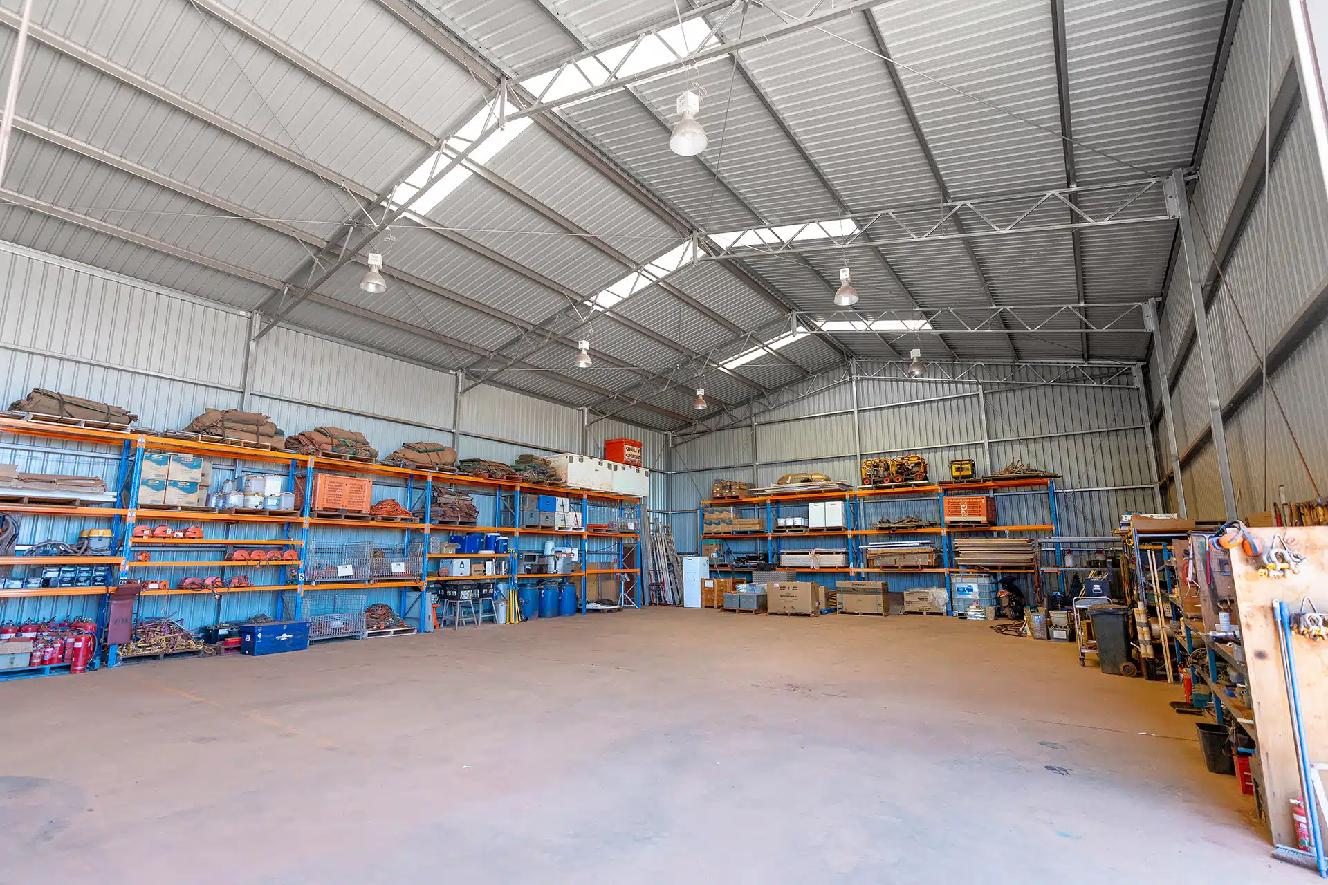 Large warehouse with metal shelves stocked with tools, safety gear, and equipment for remote site operations.