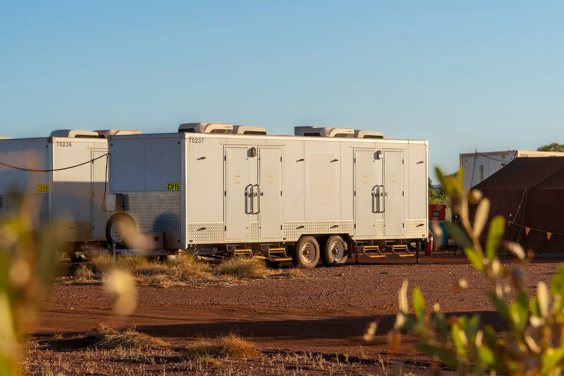 Mobile amenities block with multiple entry doors, air conditioning units, and metal steps at a remote worksite.