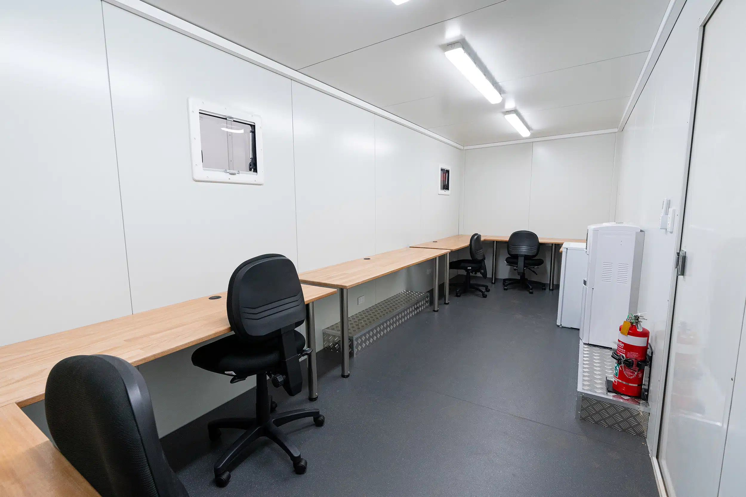 Wide view of a mobile office trailer interior with multiple desks, chairs, and essential equipment.